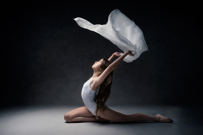 photo studio d'une danseuse classique au sol et faisant voler un voile au dessus de sa tête
