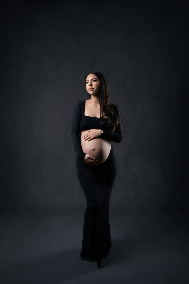 photo prise en studio d'une femme enceinte brune habillée d'une robe noire laissant dévoiler son ventre