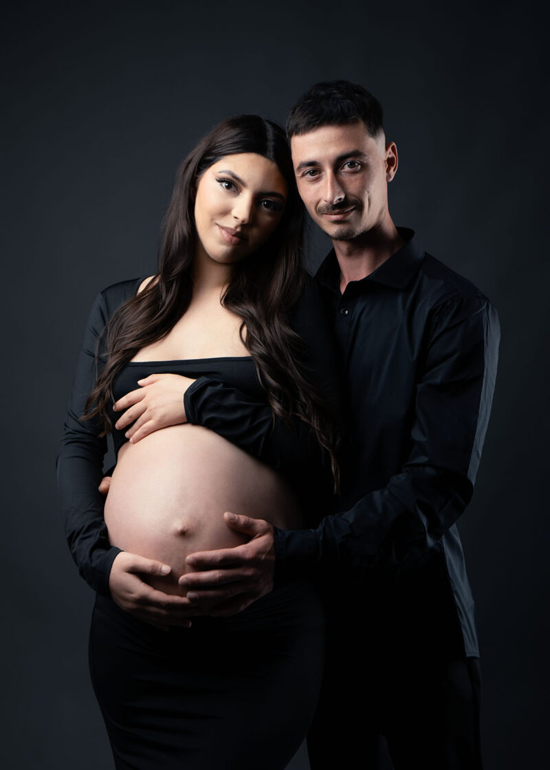 photo studio d'un couple dont la femme est enceinte et qui est habillée d'une robe noire laissant dévoiler son ventre