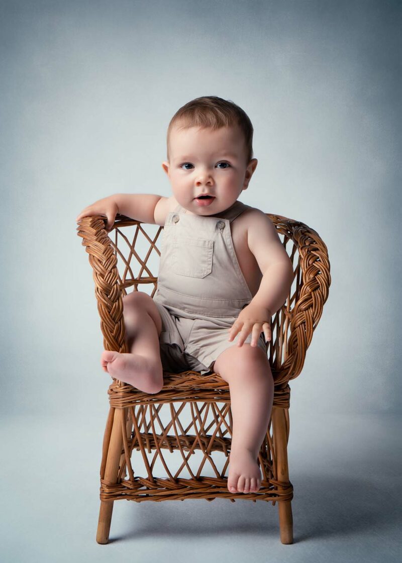 photo studio d'un petit garçon assis sur une chaise en osier
