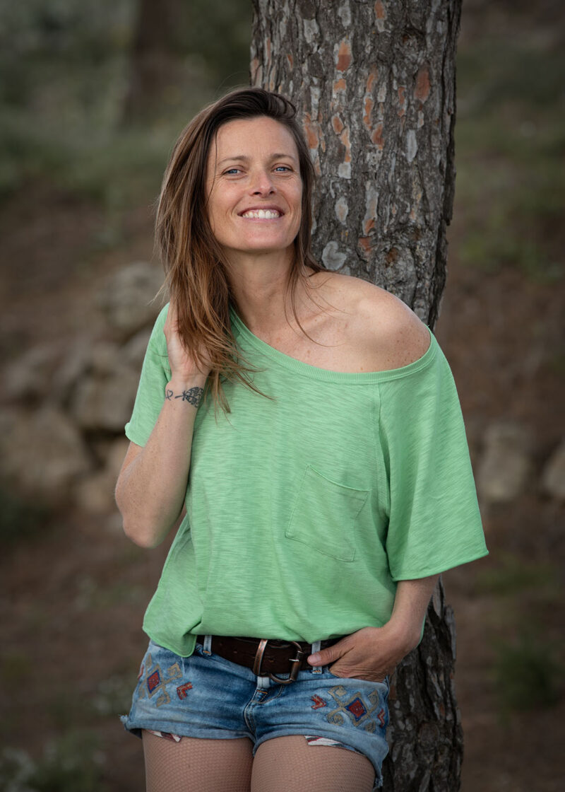 portrait en extérieur d'une femme appuyé sur un arbre habillée d'un short en jean et d'un haut vert