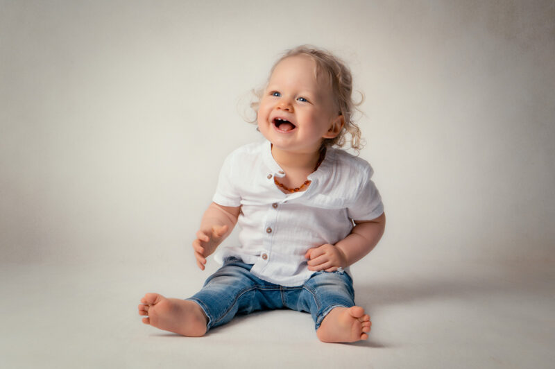 photo d'une petit enfant blond assis au sol habillé en chemise blanche et jean bleu