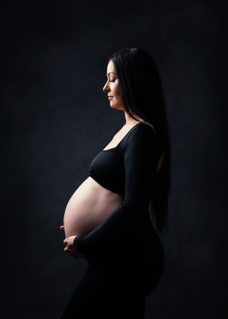 Photo studio d'une femme enceinte vue de profil portant une robe noire laissant découvrir le ventre