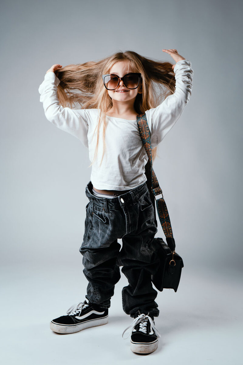 photo studio d'une petite fille portant les vêtements de sa maman et jouant avec ses cheveux