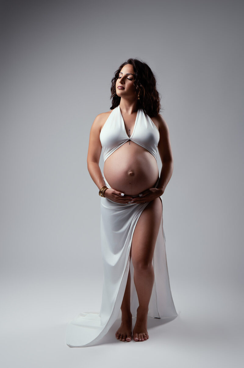 photo studio d'une robe blanche moulante d'une femme enceinte qui laisse découvrir le ventre