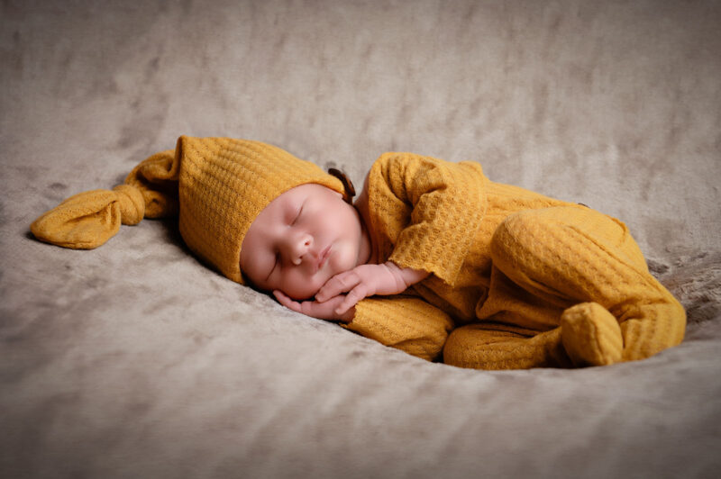 photo d'un bébé habillé avec une tenue jaune et étant allongé sur le coté les mains calées sous la tête