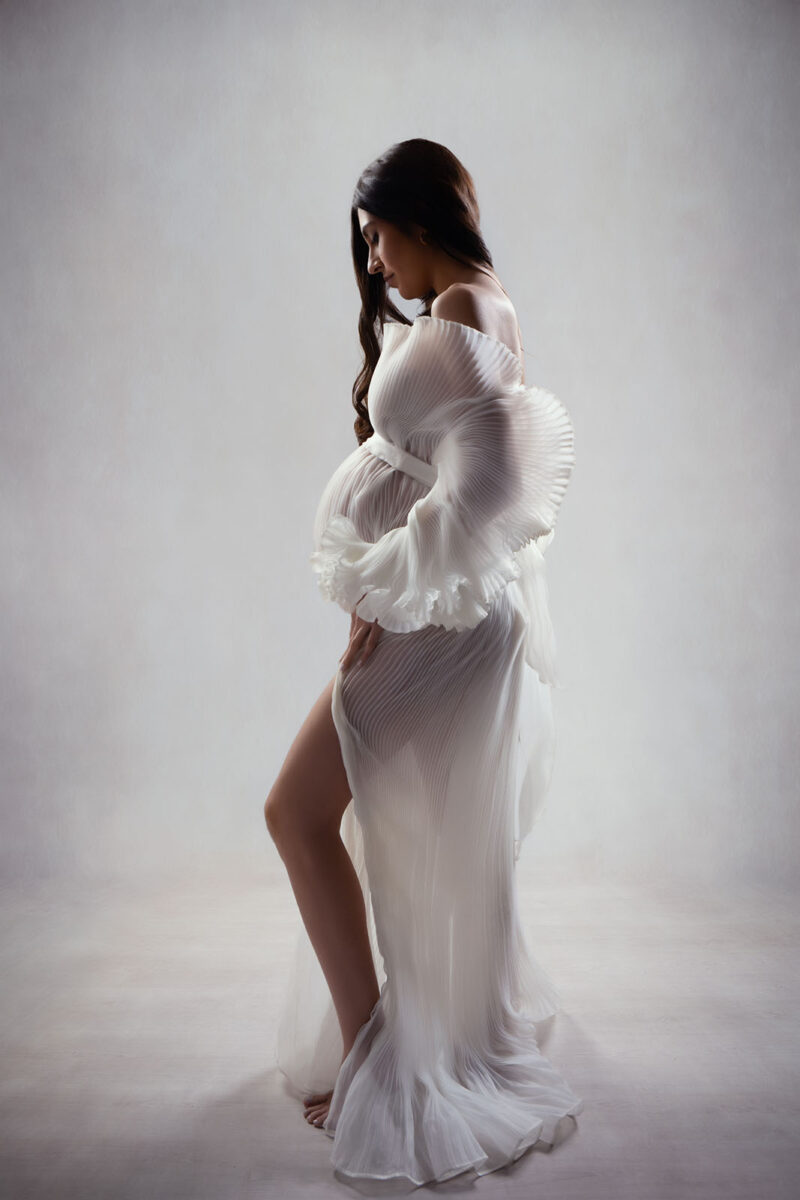 photo studio d'une femme enceinte prise de profil dans une robe blanche