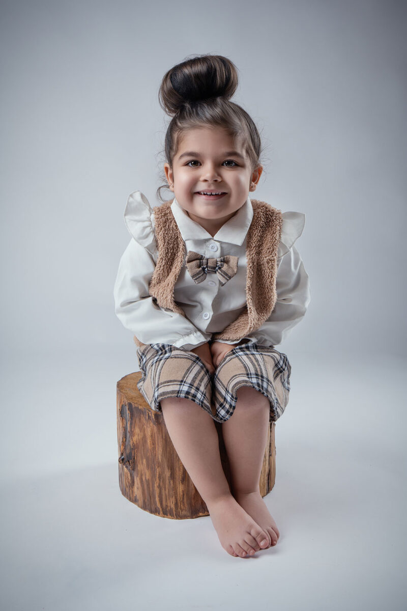 photo d'une petite fille prise en studio assise sur un petit tronc d'arbre