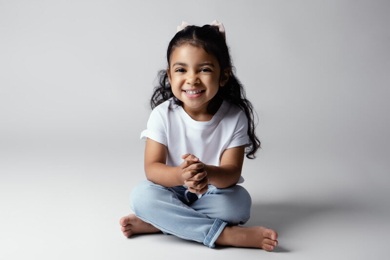 photo sur fond blanc d'une petite fille assise en tailleur au sol