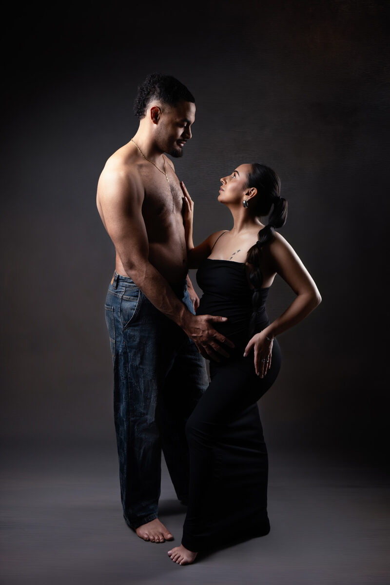 photo studio d'un couple où la femme est enceinte. Ils se tiennent en face en face, la femme à la main posée sur le torse de son conjoint