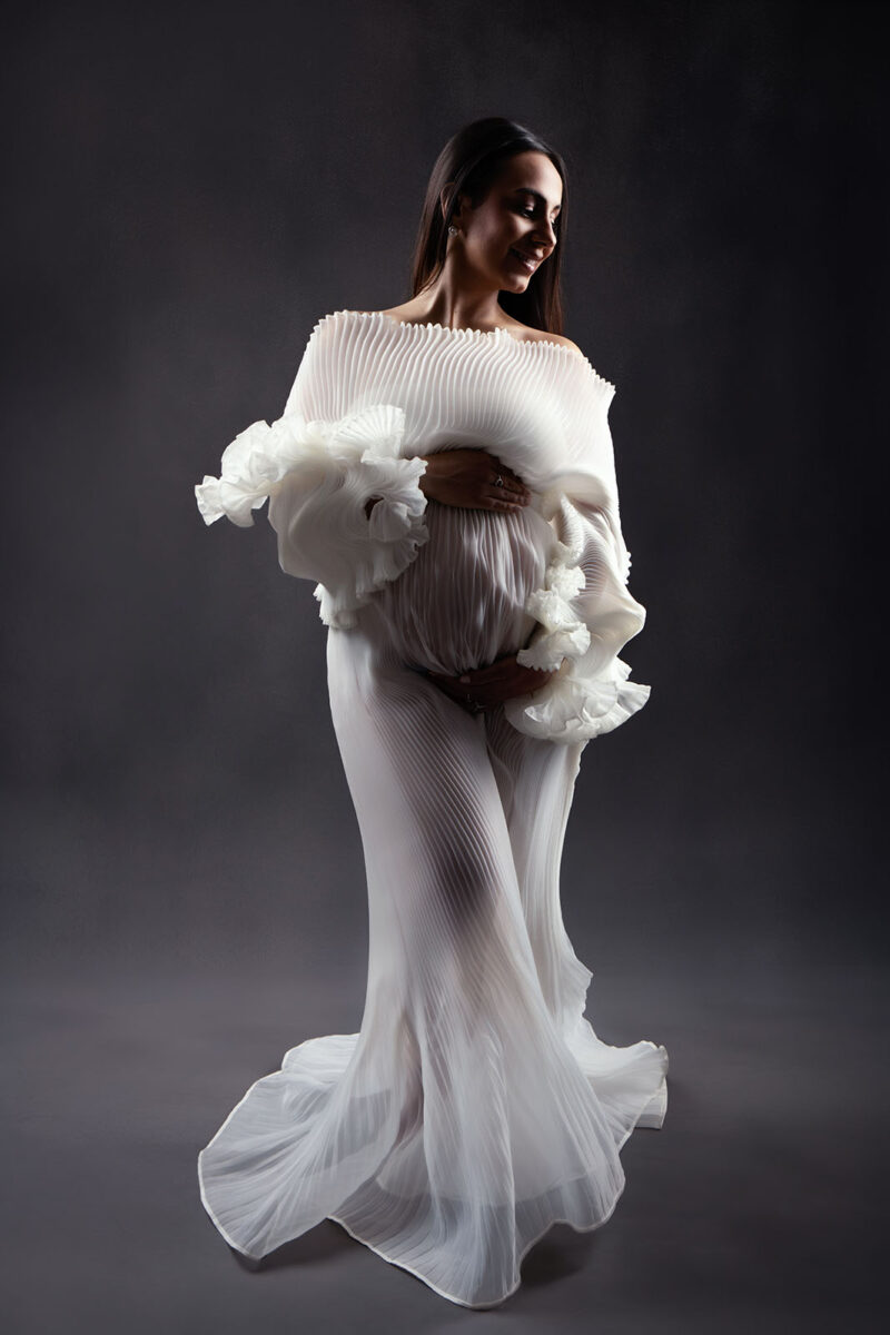 photo prise en studio d'une femme enceinte portant une robe blanche