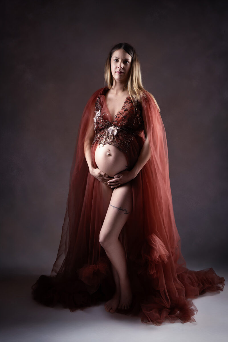 photo prise en studio d'une femme blonde enceinte portant une robe en tulle ouverte sur le ventre.