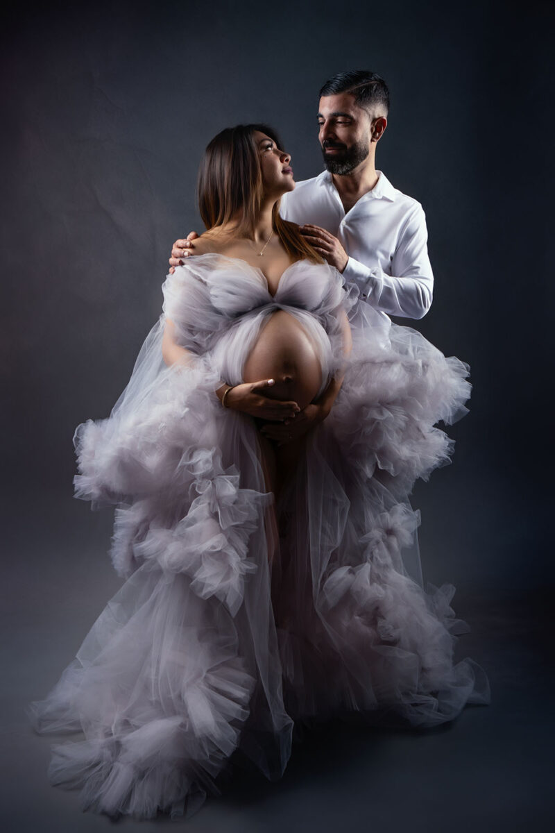 photo studio d'un couple dont la femme est enceinte et porte une robe en tulle